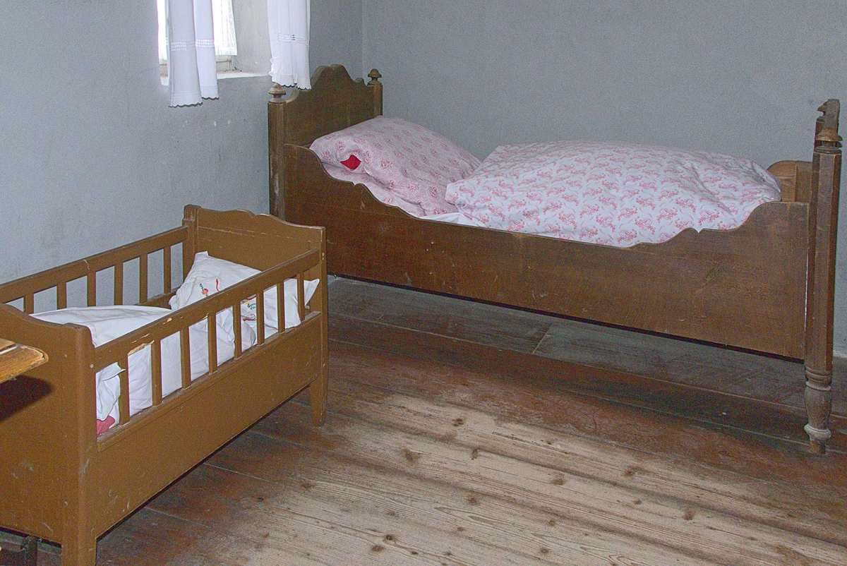 Chambre aménagée avec un lit adulte et un petit berceau en bois clair pour enfant
