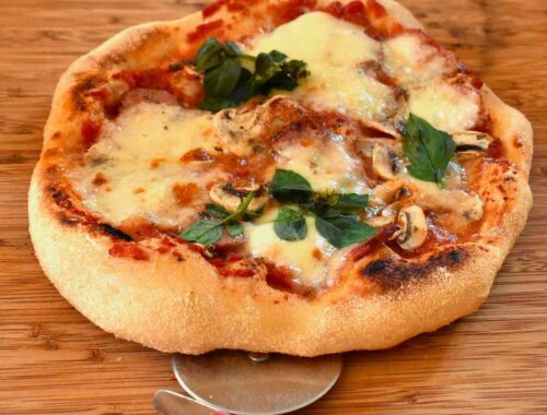Pizza au fromage, basilic, champignons sur planche, coupe-pizza à côté