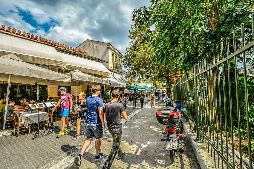 ALT: rue animée avec cafés en terrasse, piétons et une moto ALT: rue animée avec cafés en terrasse, piétons et une moto