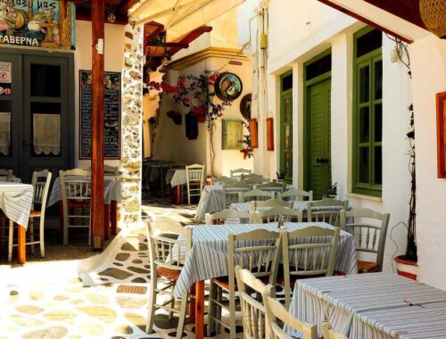 Courtyard restaurant with striped tablecloths, wooden chairs, stone pavement, green doors