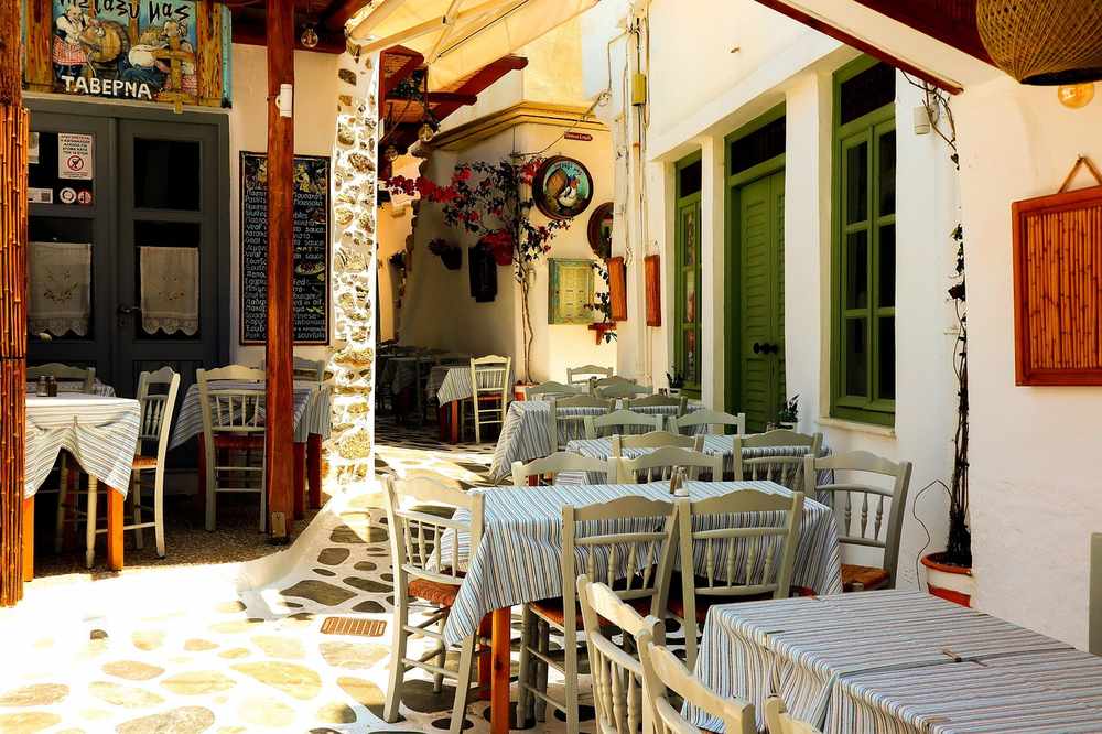 Courtyard restaurant with striped tablecloths, wooden chairs, stone pavement, green doors